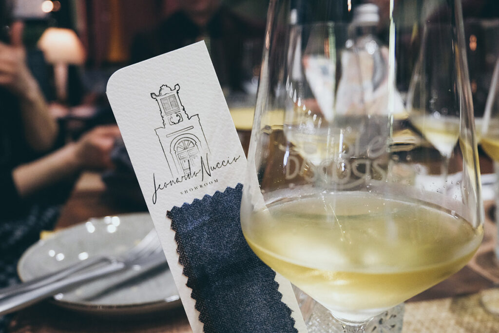 Calice di vino bianco Conti Zecca accanto a segnalibro Leonardo Nuccio Showroom personalizzato con tessuto